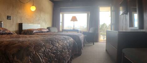A hotel room with a large bed, a desk, and a chair. There is a window with curtains and a view of the outside.