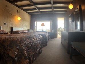 A hotel room with a large bed, a desk, and a chair. There is a window with curtains and a view of the outside. - Fountain Inn (Bucksport)
