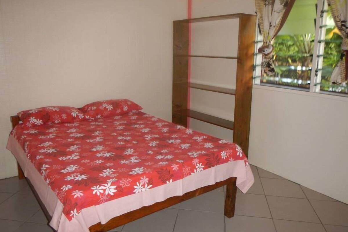 A bedroom with a bed, a window with curtains, and a view of greenery outside.