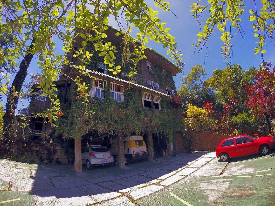 Um edifício com telhado verde, cerca branca e um carro vermelho estacionado em frente.