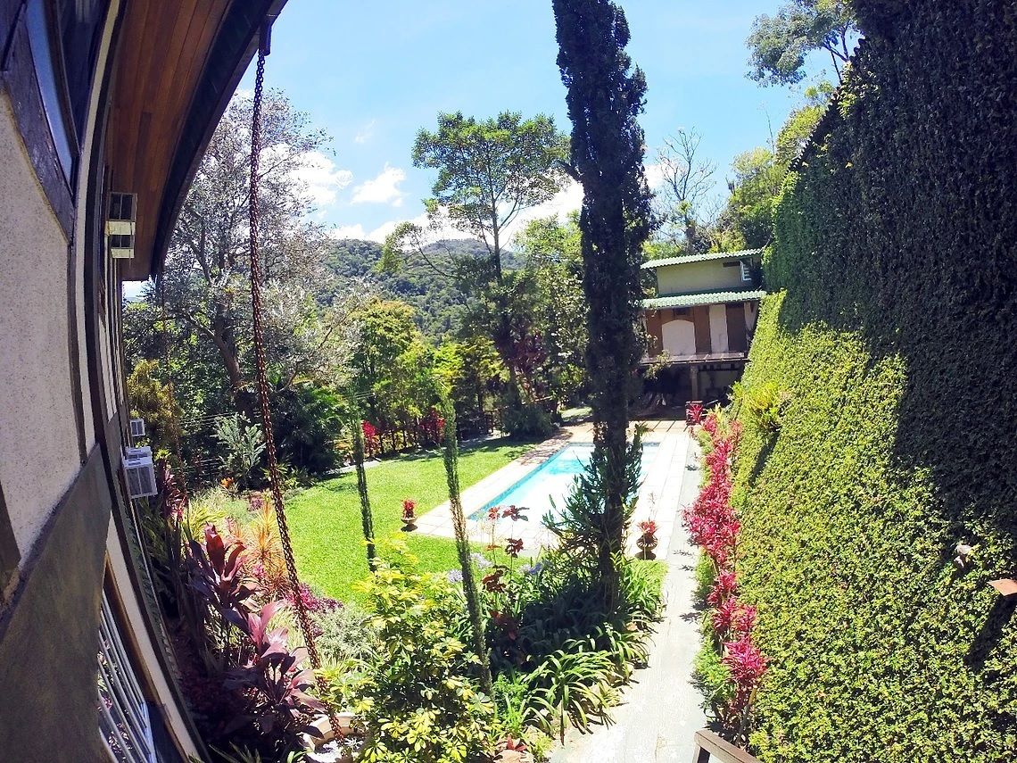 A garden with a swimming pool, surrounded by lush greenery and a building with a tiled roof.