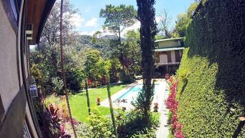 A garden with a swimming pool, surrounded by lush greenery and a building with a tiled roof.