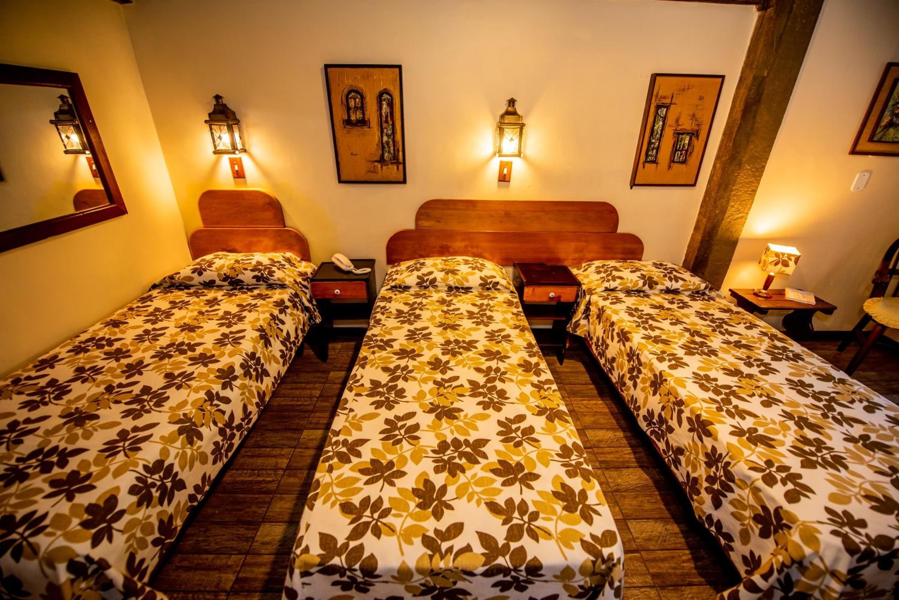 Ein Hotelzimmer mit zwei Einzelbetten, jeweils mit floralem Bettbezug, einem hölzernen Kopfstück, Nachttischen mit Lampen und Wandleuchten.