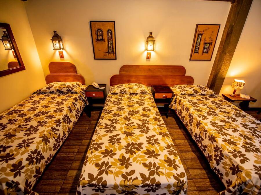 Ein Hotelzimmer mit zwei Einzelbetten, jeweils mit floralem Bettbezug, einem hölzernen Kopfstück, Nachttischen mit Lampen und Wandleuchten.