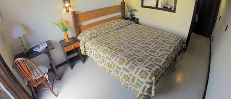 Un dormitorio con una cama grande, una silla de madera, un escritorio con una lámpara y un espejo en la pared.