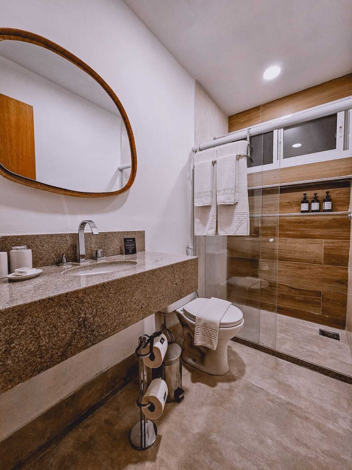 A modern bathroom with a granite countertop, a toilet, a shower with a glass door, and a wooden vanity.