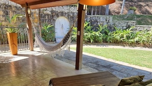 Un espacio al aire libre cubierto con una hamaca, un banco de madera y una planta en maceta.