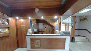 A reception area with a wooden counter, tiled floor, and a staircase in the background. - Hotel St. John (Blumenau)