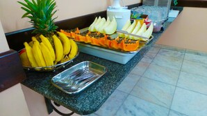 A buffet counter with a variety of fruits including bananas, pineapple, and papaya. - Hotel St. John (Blumenau)