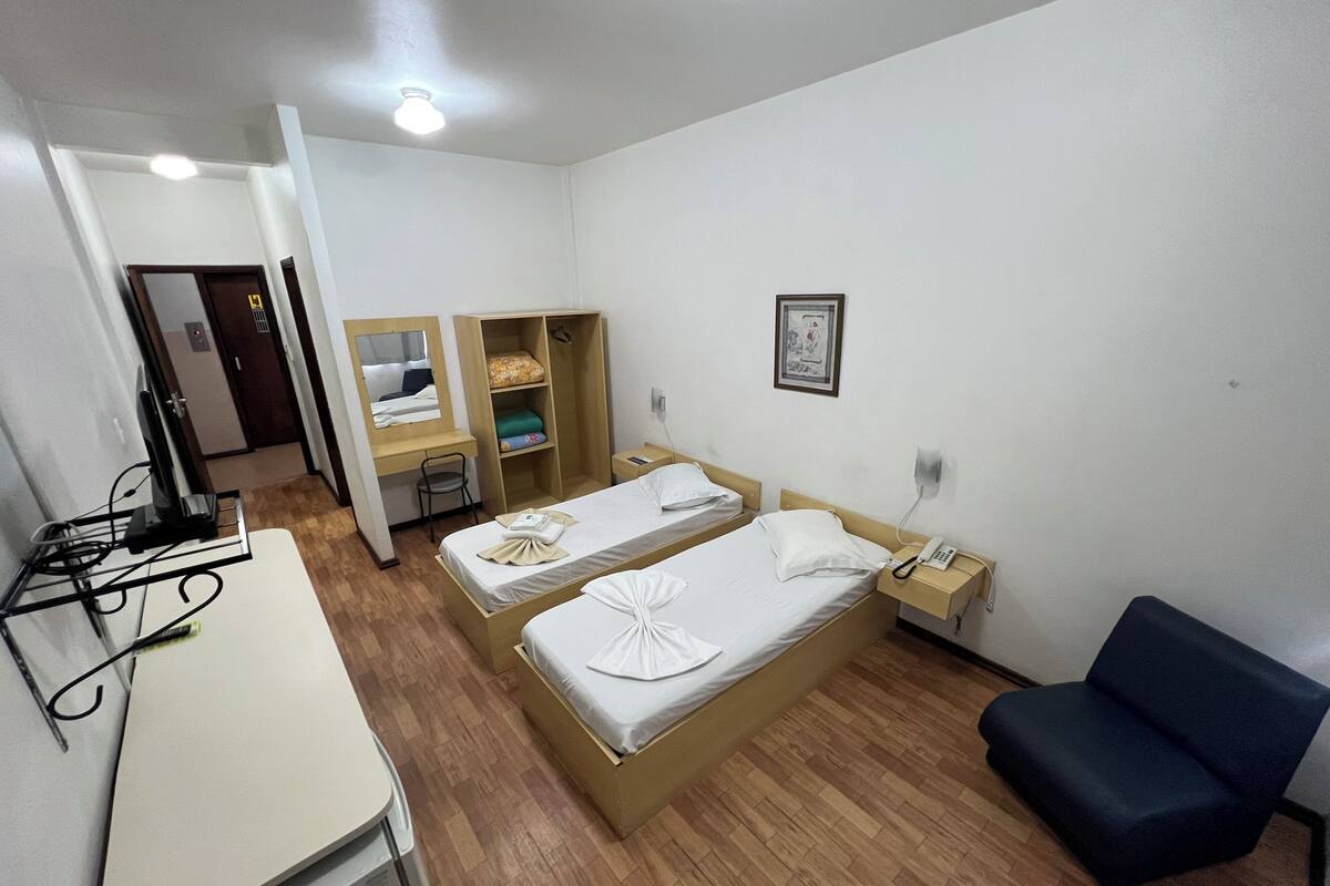 Habitación de hotel con dos camas, un escritorio, una silla, un armario y un teléfono en la mesita de noche.