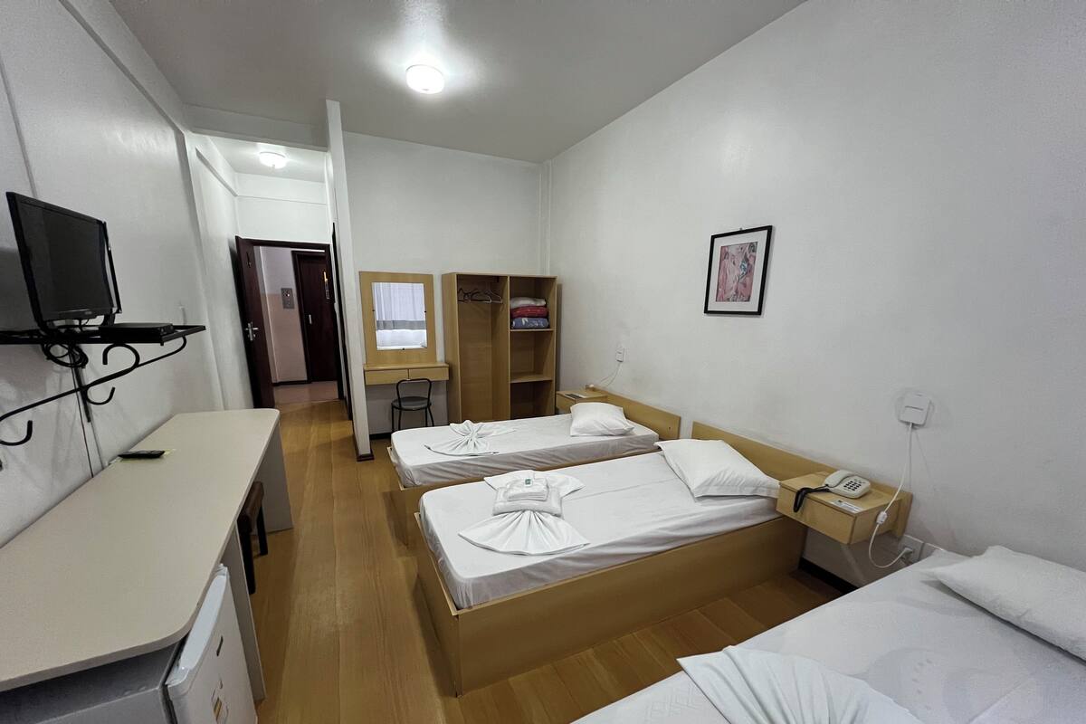 Una habitación de hotel con dos camas, un escritorio, un televisor, un armario y la puerta del baño.