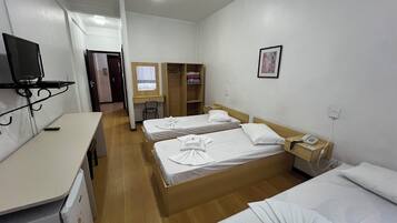 Una habitación de hotel con dos camas, un escritorio, un televisor, un armario y la puerta del baño.