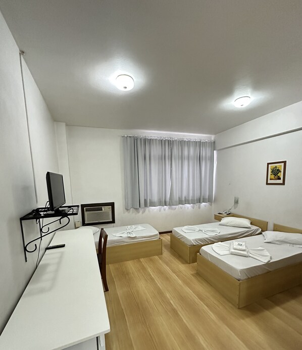 Una habitación de hotel con escritorio, dos camas, televisor y ventana con cortinas.