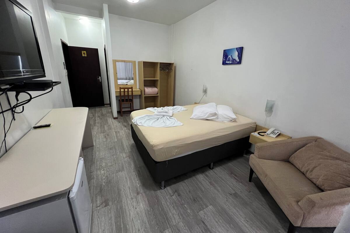 Una habitación de hotel con cama, escritorio, televisor, armario y sofá.
