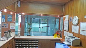 A reception desk with a computer, a clock, and various informational signs. - Hotel St. John (Blumenau)
