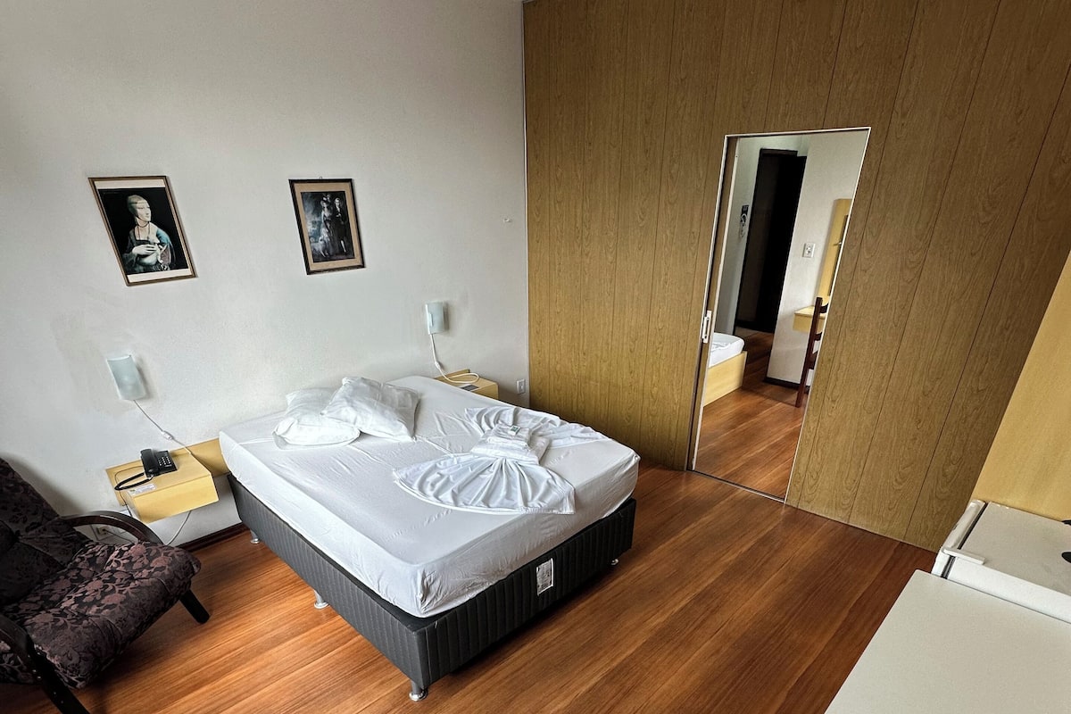 Un dormitorio moderno con una cama grande, suelo de madera, una mesita de noche con lámpara y dos cuadros en la pared.