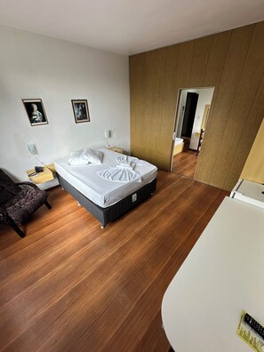 Una camera da letto moderna con un letto grande, pavimento in legno, un comodino con una lampada e due quadri appesi al muro.