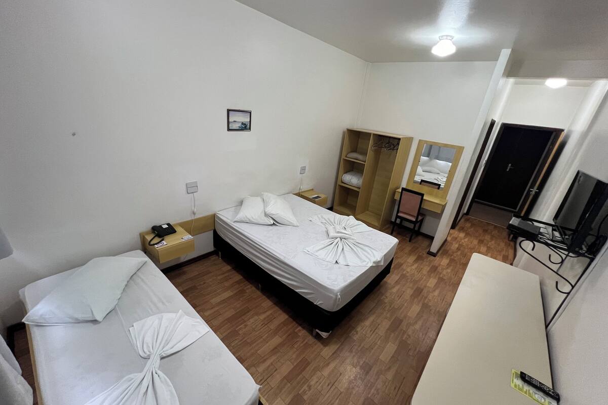 Habitación de hotel con dos camas, un armario, un escritorio con silla, un espejo y un televisor.