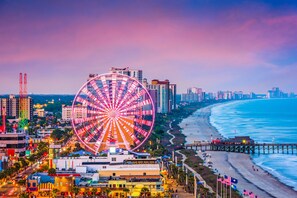 A coastal cityscape with a prominent Ferris wheel, beachfront, and a pier.