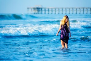Eine Person steht im Meer, Wellen im Hintergrund.
