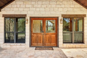 Un edificio de piedra con una puerta doble de madera, dos ventanas con marcos negros y un felpudo con la palabra 'HELLO'.