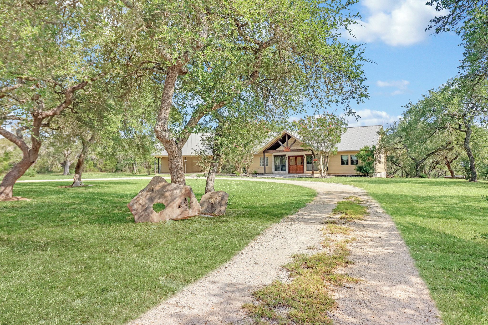 A house with a gravel driveway, surrounded by trees and grass.