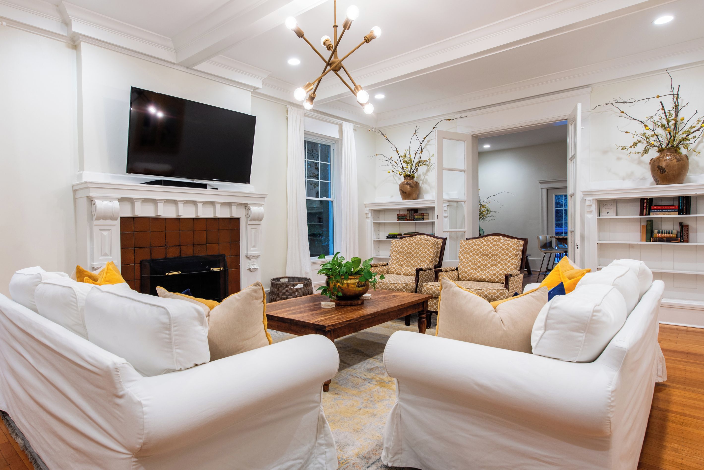 Una sala de estar con sofás blancos, chimenea, televisor y candelabro.