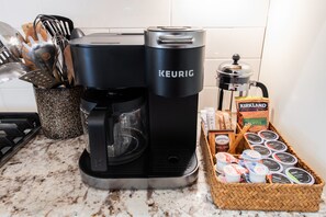 A Keurig coffee maker on a kitchen counter with a coffee pot, utensils, and a basket of coffee pods.