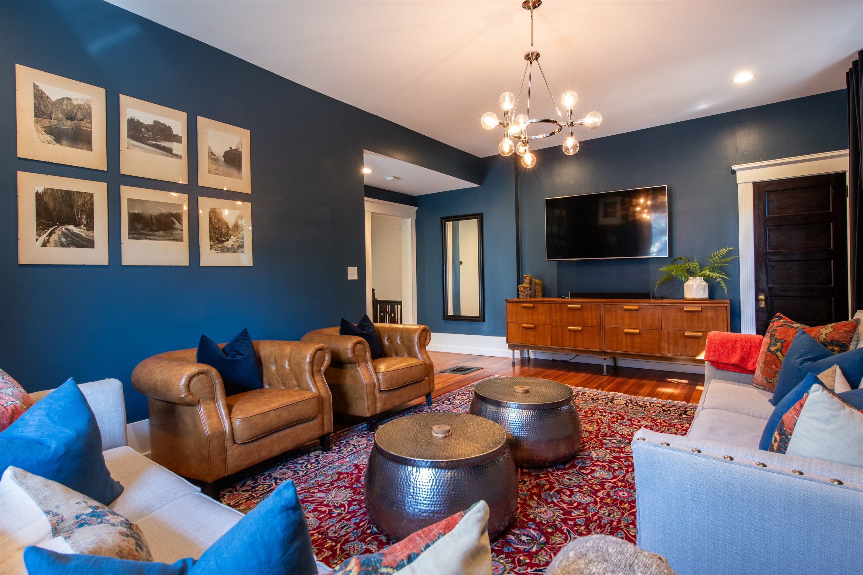 A living room with a blue wall, leather sofas, a patterned rug, and a wooden cabinet.