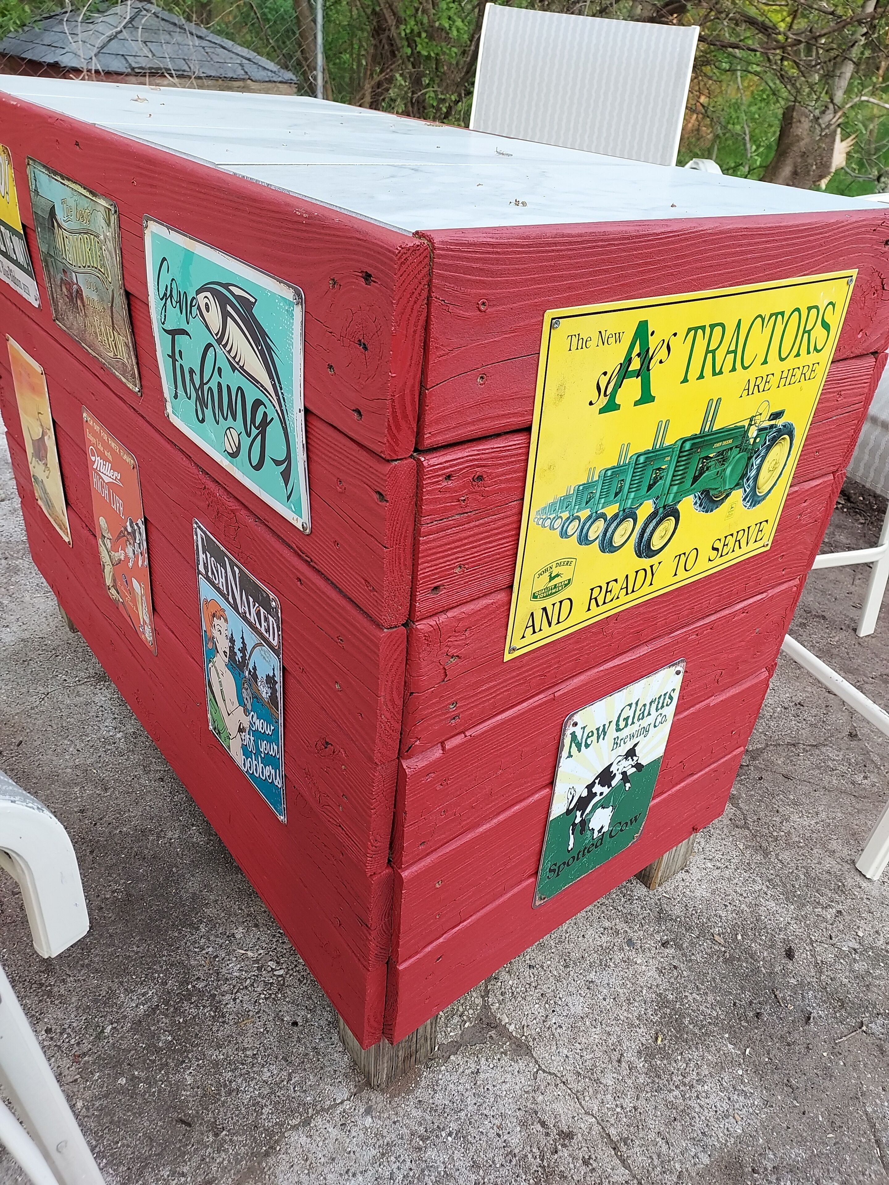 Een rode houten constructie met verschillende oude reclameborden en advertenties, waaronder een voor 'The New A Tractors' en 'New Glarus Brewing Co.'