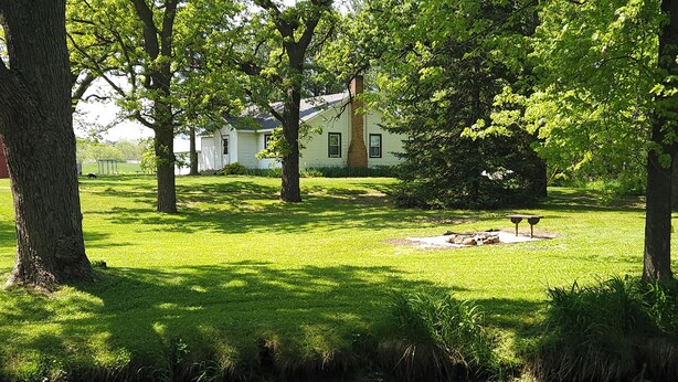 Un parc paisible avec un étang, une pelouse verdoyante et une maison en arrière-plan.