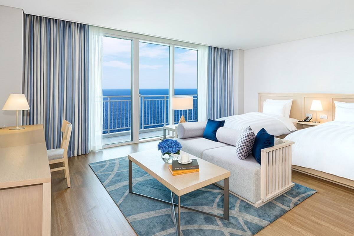 Une chambre d’hôtel avec un grand lit, un canapé, un bureau et une vue sur l’océan.
