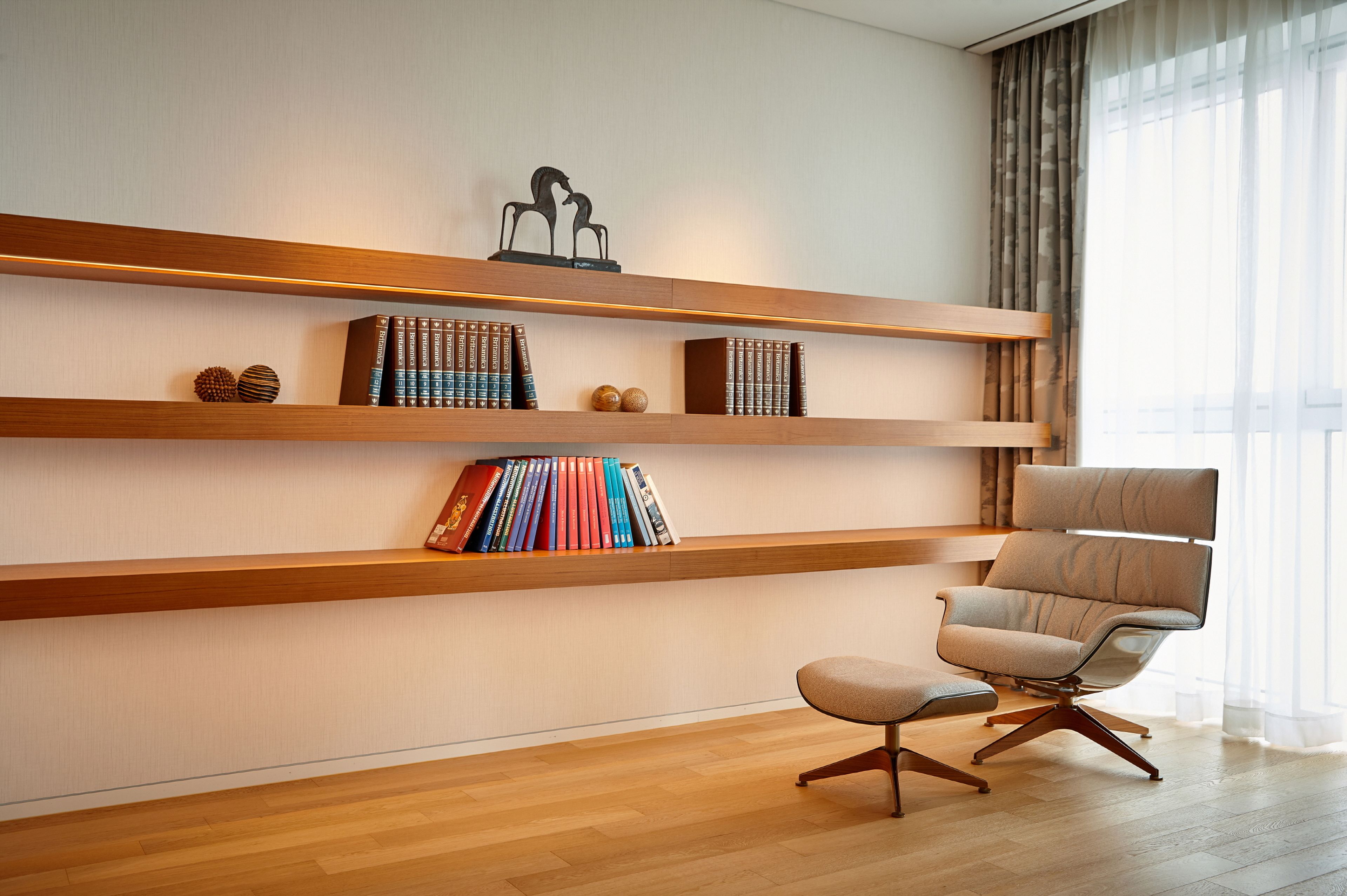A modern living room with wooden shelves, a comfortable armchair, and a small ottoman.