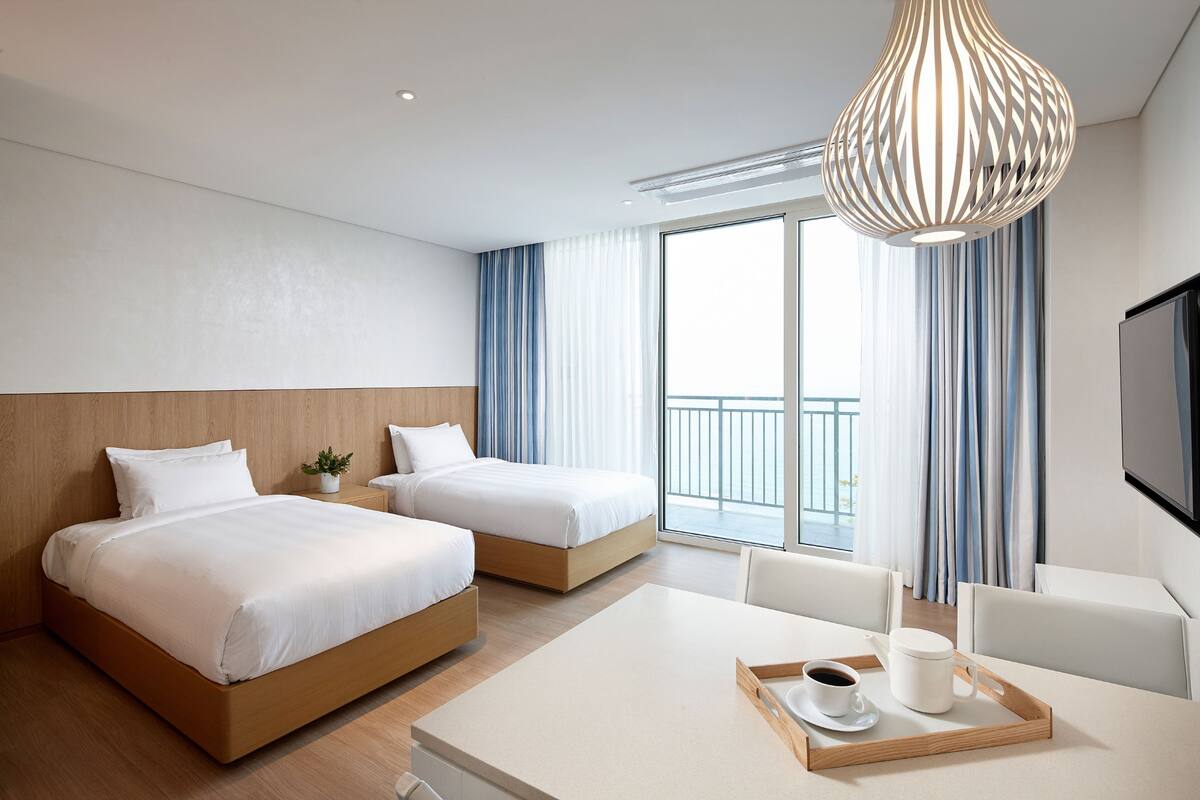 Une chambre d’hôtel avec deux lits, une table à manger sur laquelle se trouve un plateau avec du café, et un téléviseur fixé au mur.