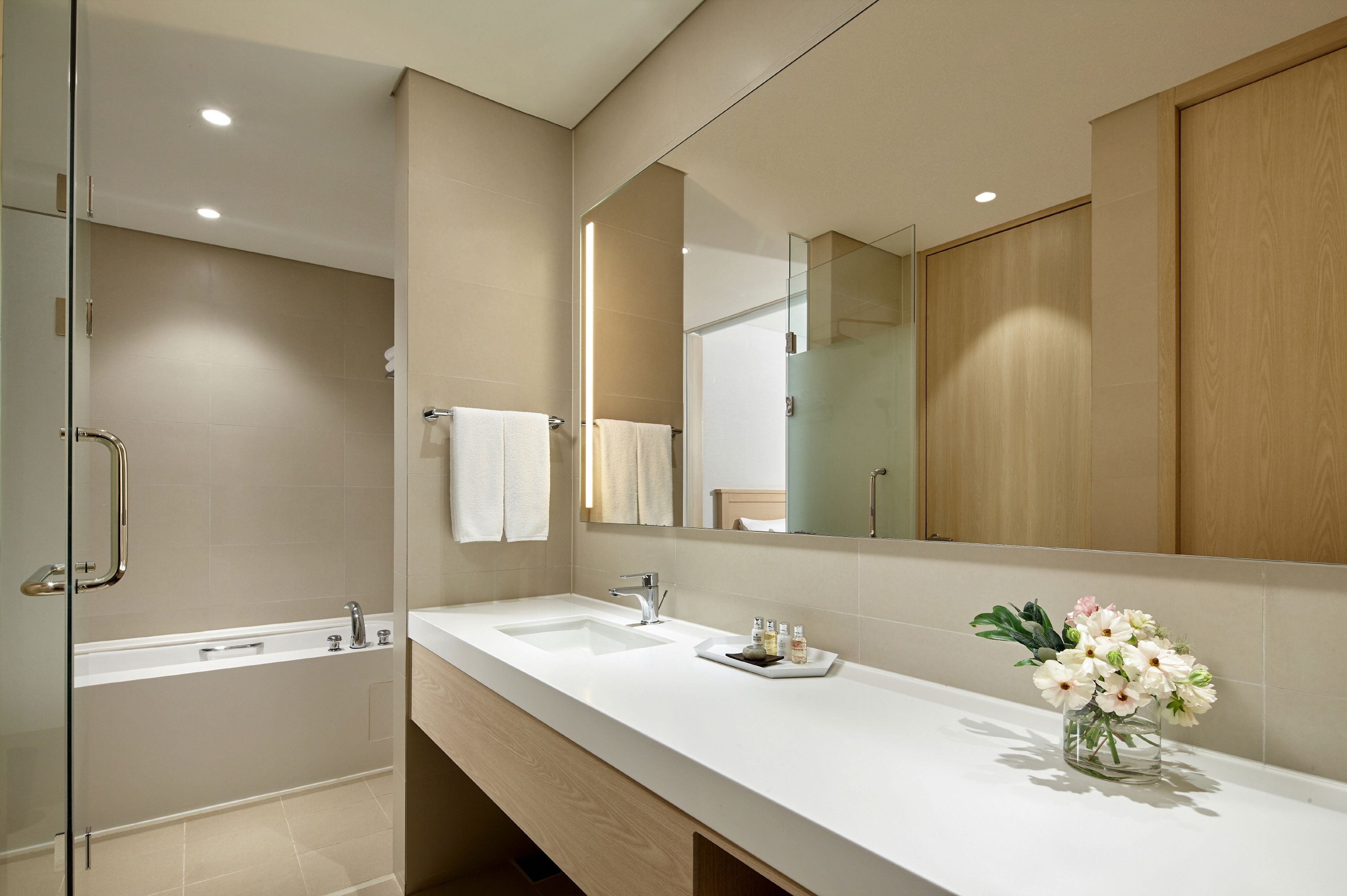 A modern bathroom with a glass shower enclosure, a large mirror, and a white vanity with a vase of flowers.