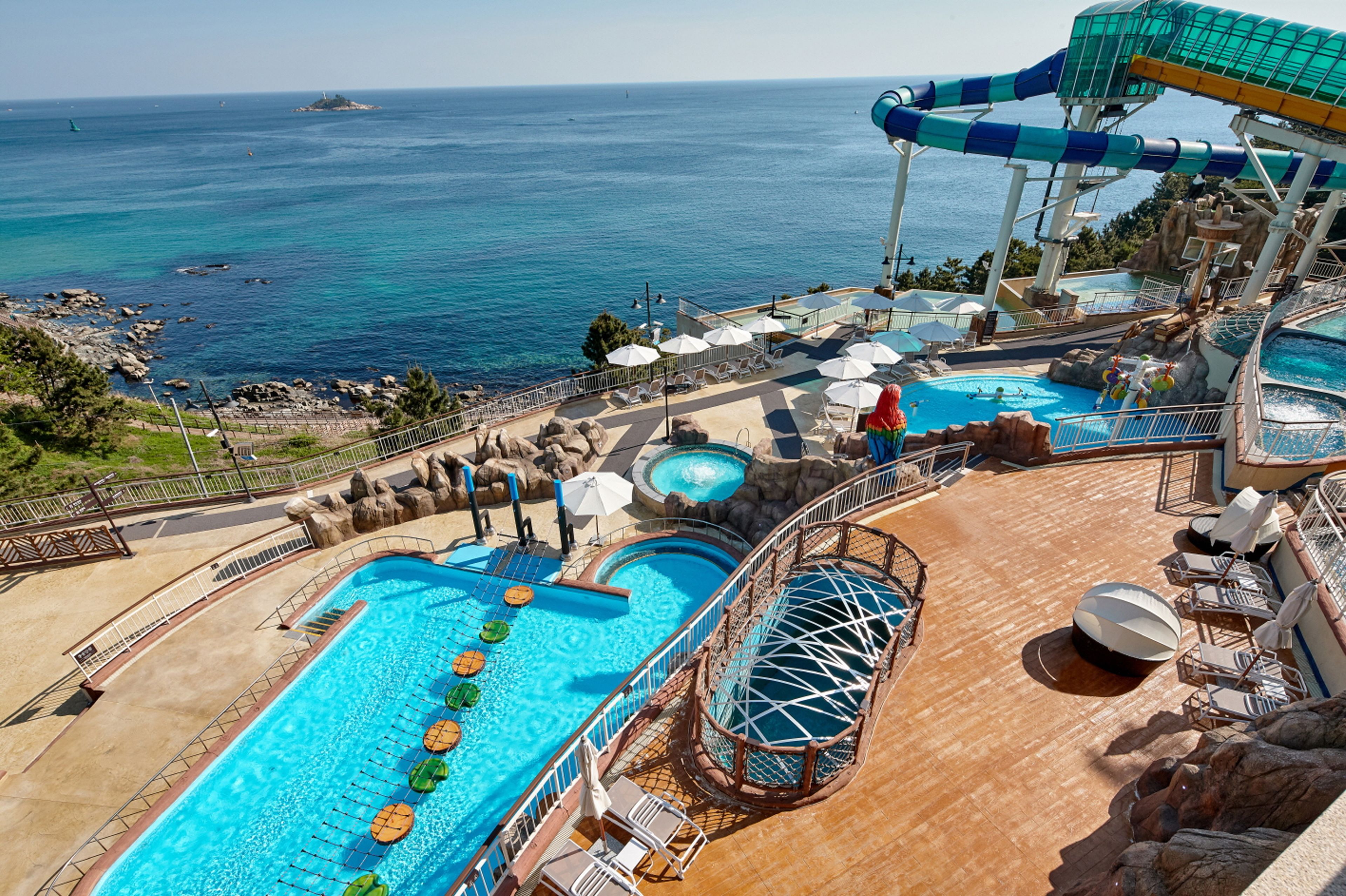 A cruise ship deck with multiple swimming pools, a water slide, and lounge areas.
