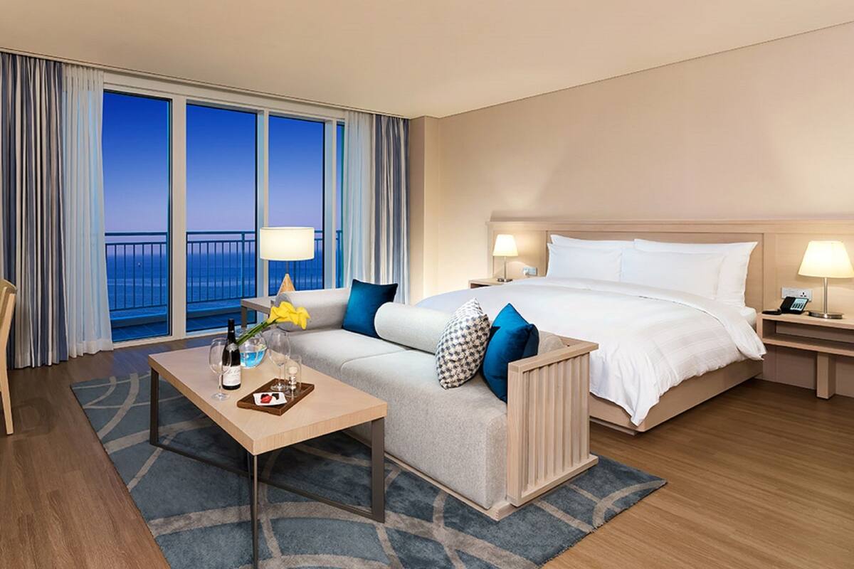 Une chambre d’hôtel avec un grand lit, un canapé, un bureau et une vue sur l’océan.