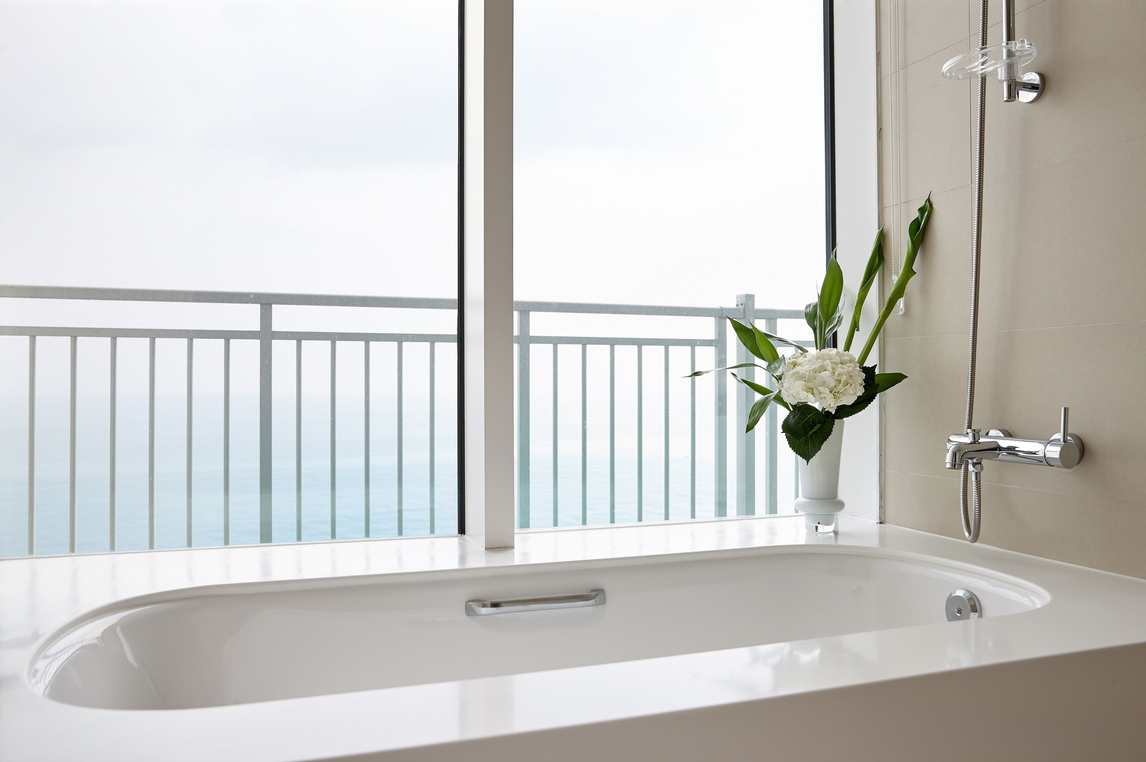 A modern bathroom with a large bathtub, a shower, and a view of the sea through a balcony.