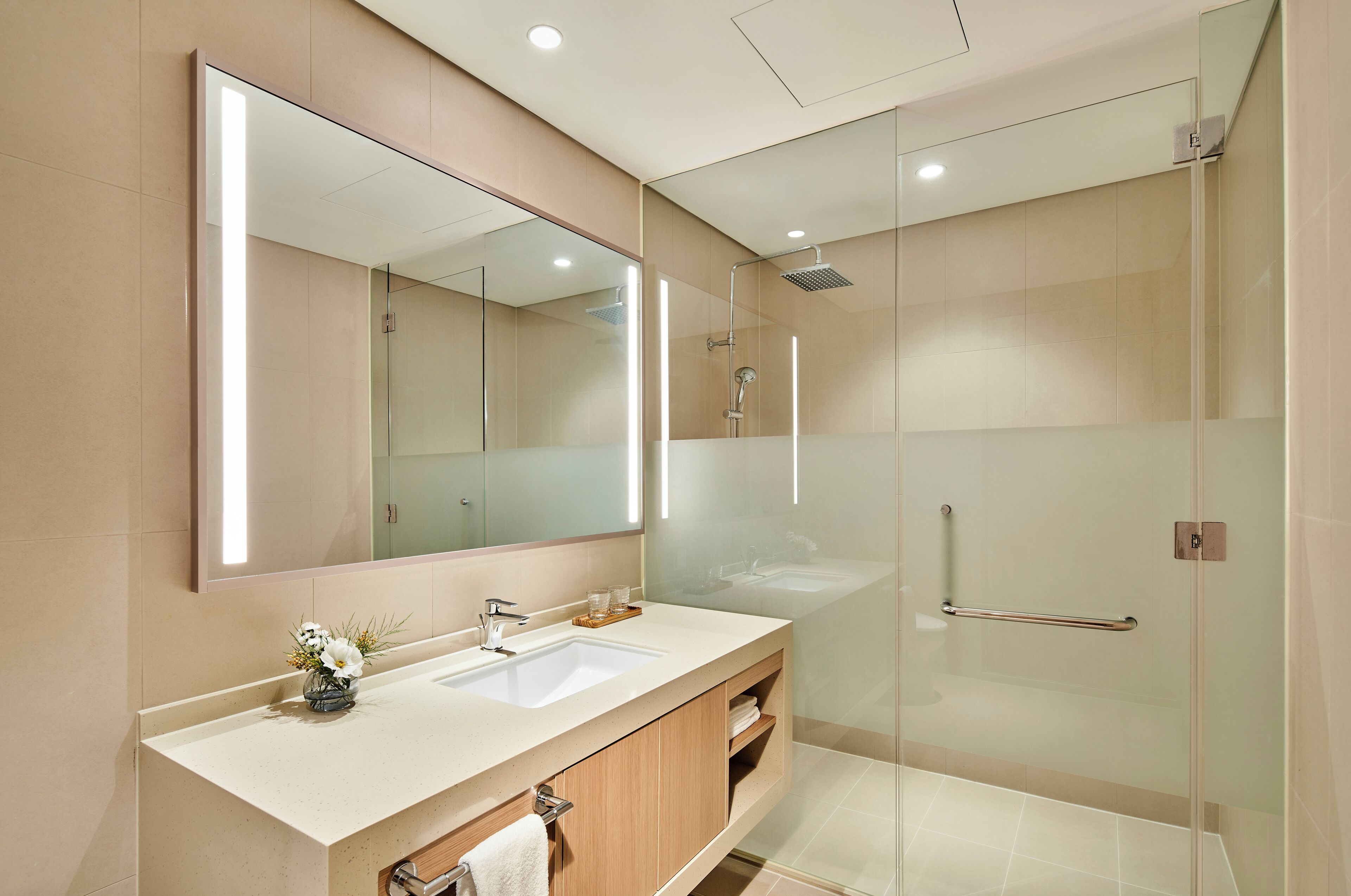 A modern bathroom with a large mirror, two sinks, a shower, and a glass-enclosed shower area.