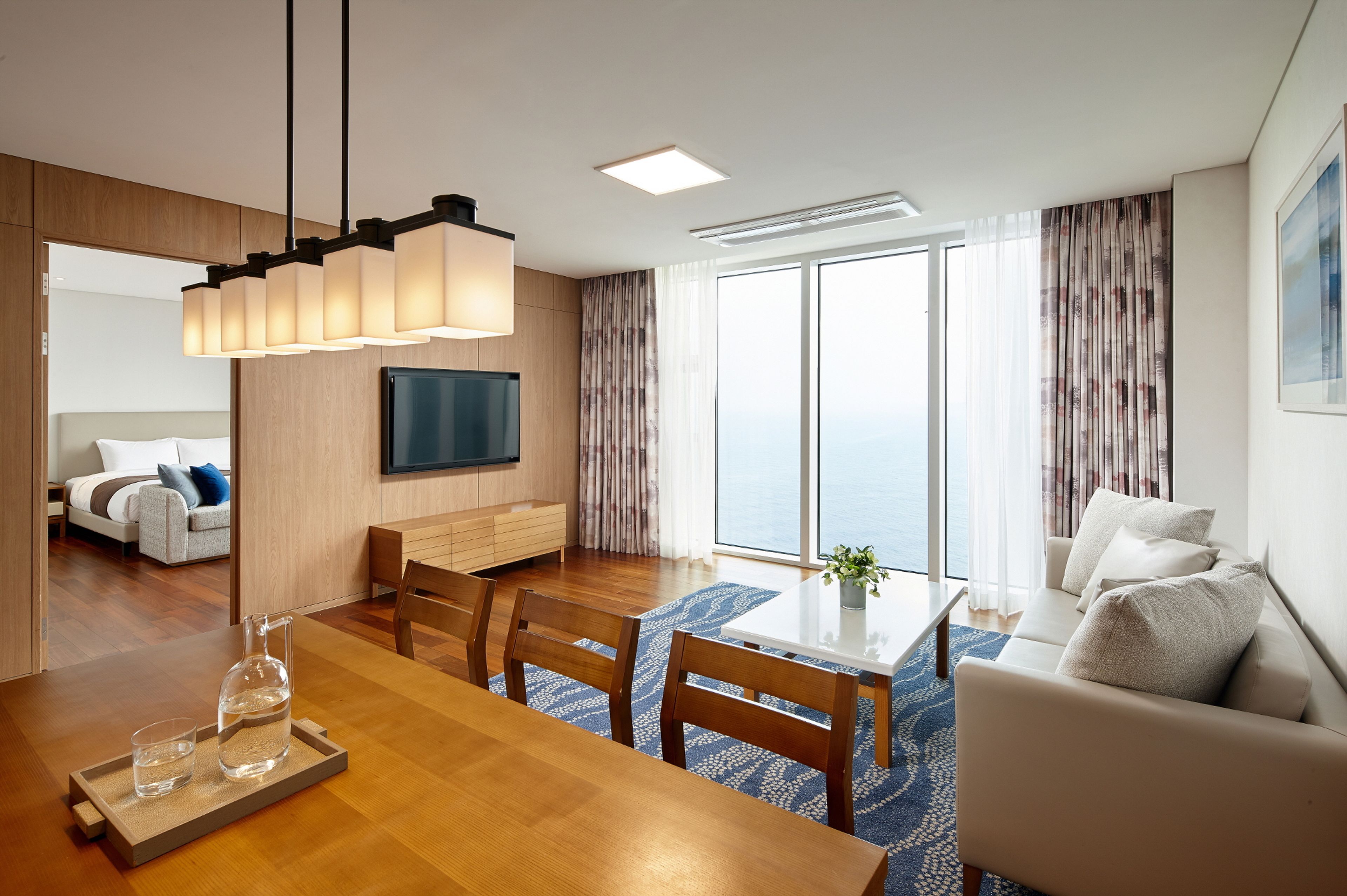 Habitación de hotel moderna con zona de comedor, sofá y un ventanal con vistas al mar.