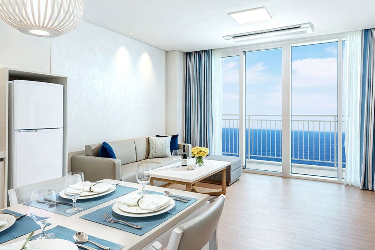 Une chambre d’hôtel moderne dotée d’un coin repas, d’un canapé, d’une télévision et d’un balcon avec vue sur la mer.