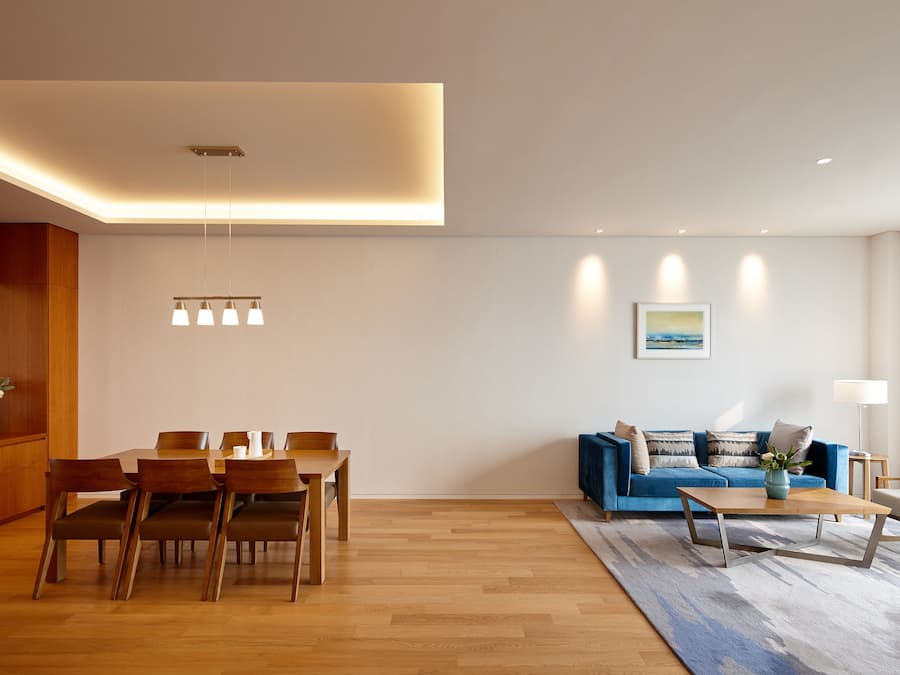Een moderne woonkamer met een eethoek, met een houten eettafel, stoelen, een blauwe bank en een salontafel.