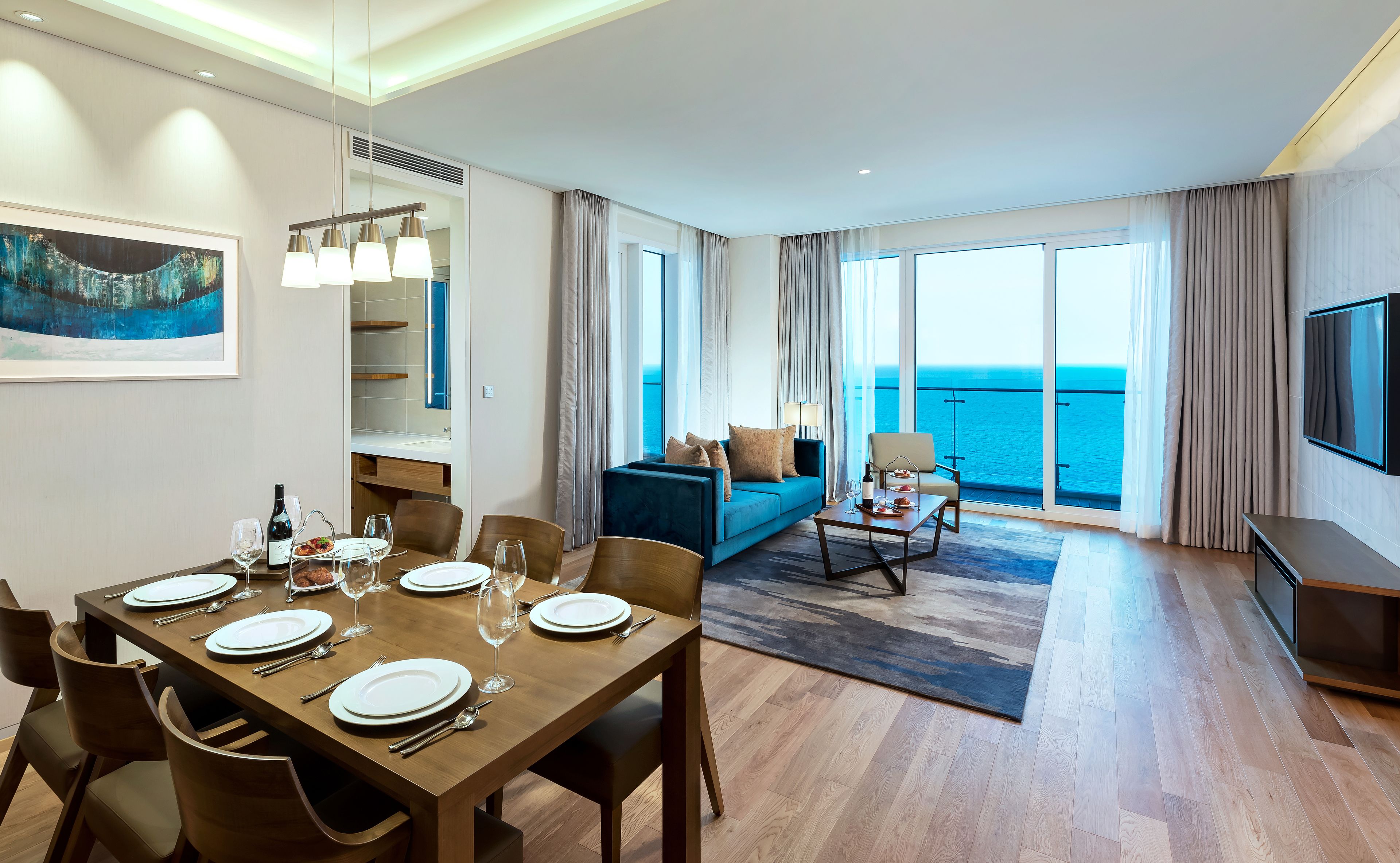 Una habitación de hotel moderna con zona de comedor, sofá y vista al mar.