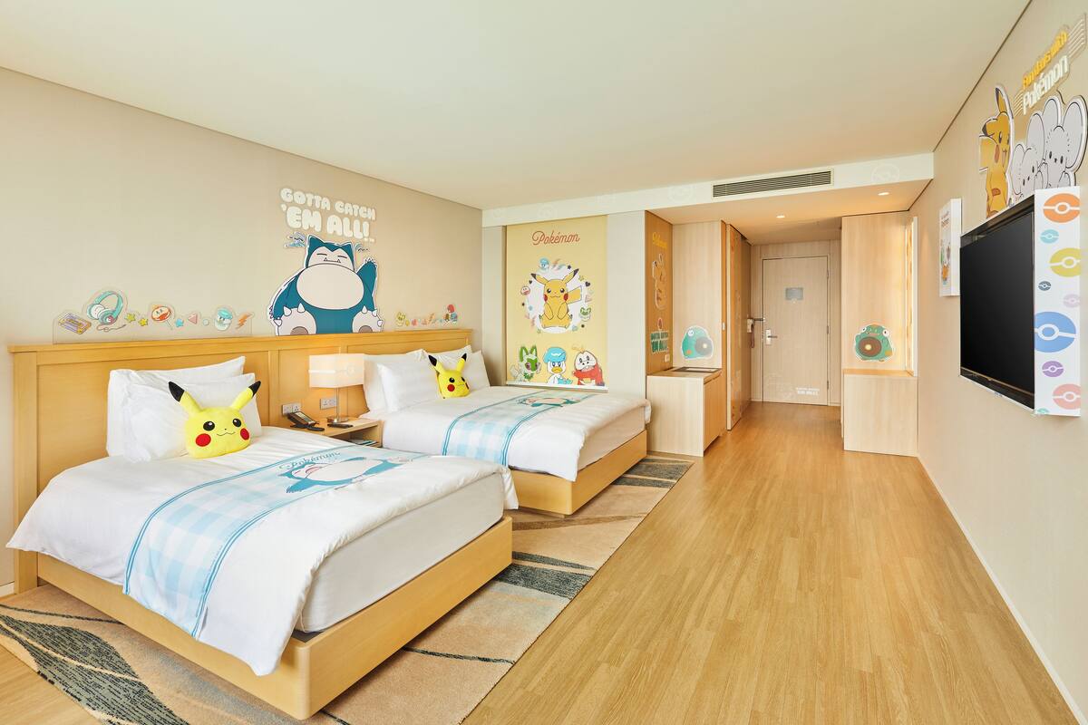 Une chambre d’hôtel avec deux lits, une télévision et une décoration sur le thème de Pokémon.