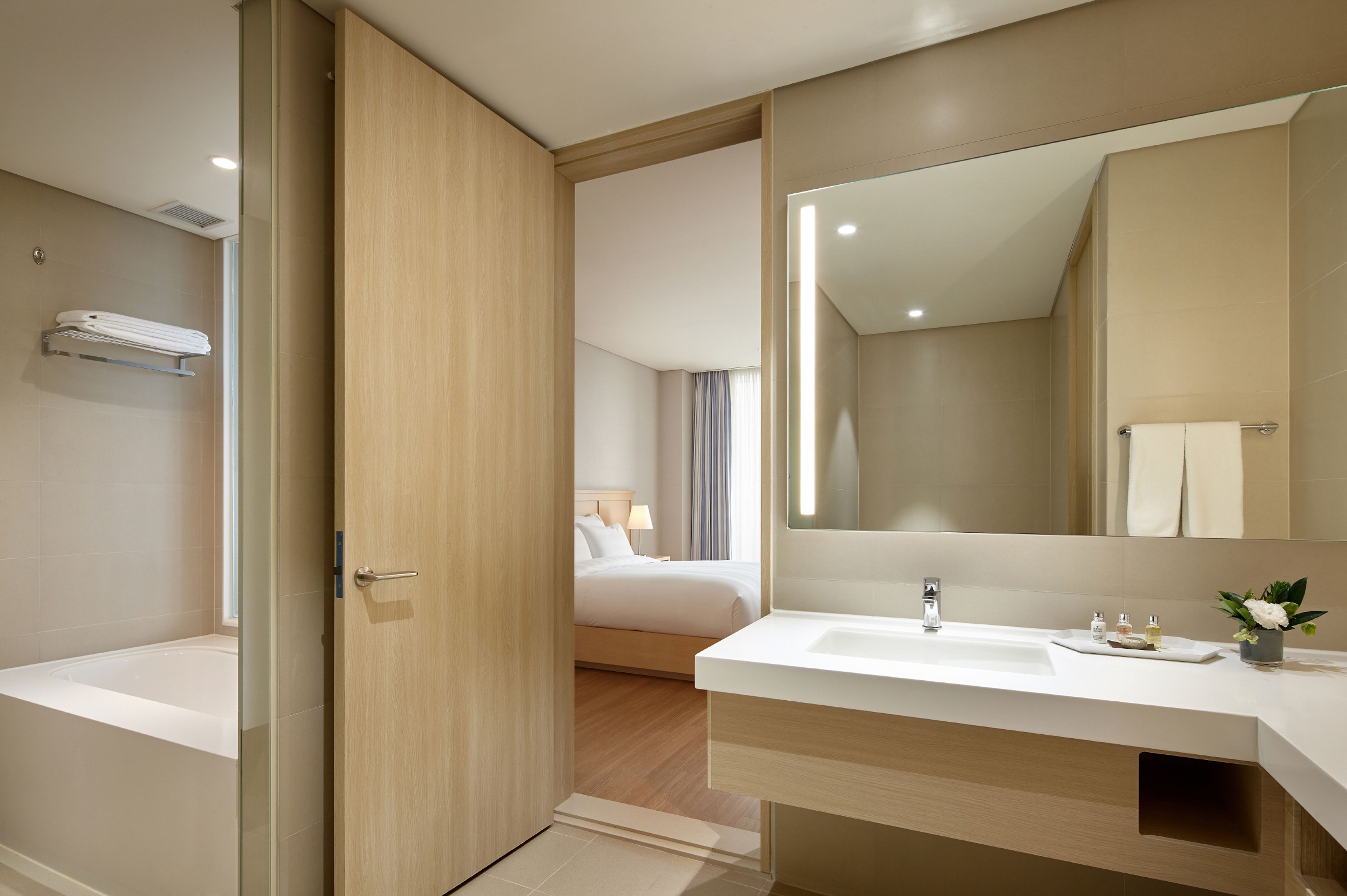 Un bagno moderno in hotel con uno specchio grande, una vasca, un lavandino e una doccia.