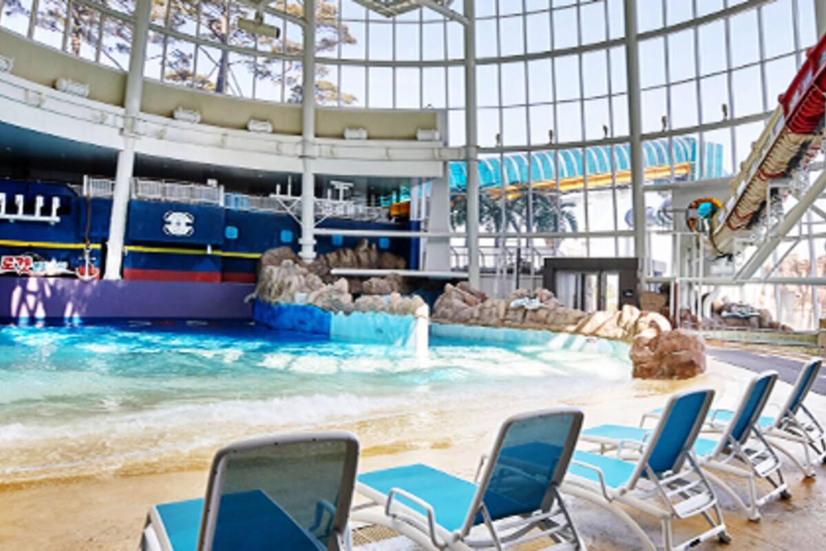 Une piscine intérieure dotée d’un toboggan, de chaises longues et offrant une vue sur l’océan grâce à de grandes fenêtres.