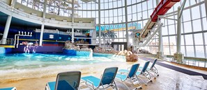 Una piscina interior con tobogán de agua, sillas de descanso y vistas al océano a través de amplias ventanas.