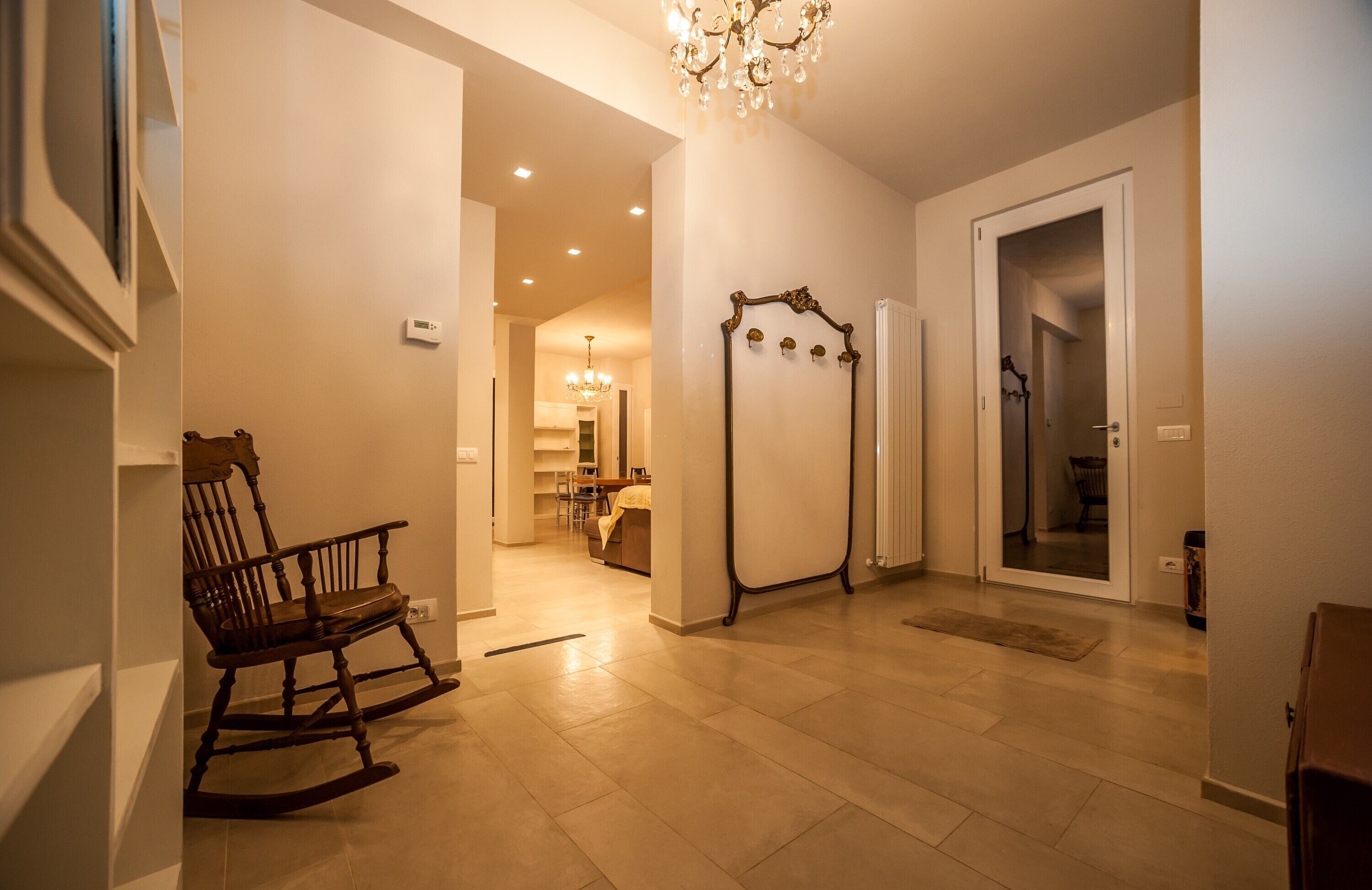 A hallway with a wooden rocking chair, a chandelier, and a radiator.