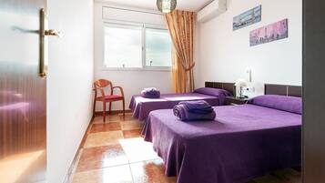 A hotel room with two beds, a chair, a window with curtains, and artwork on the wall.