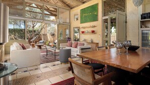 A spacious room with a high ceiling, large windows, and a wooden dining table.